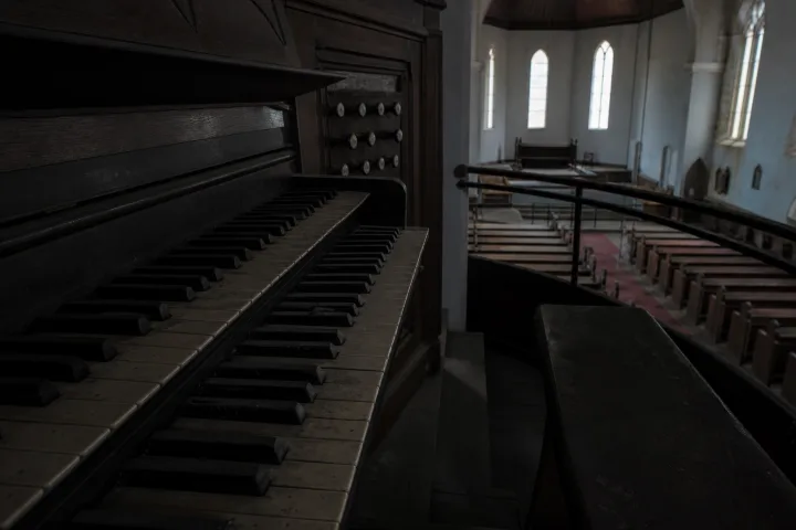 Vecchio organo da chiesa in penombra con panche vuote e luce fredda
