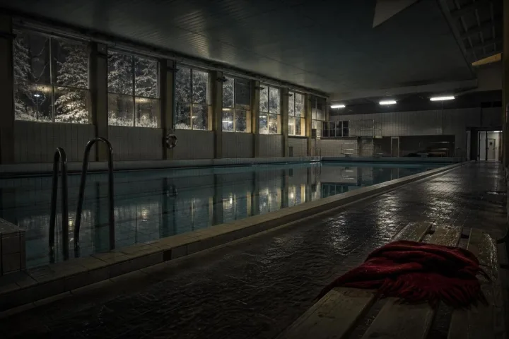 Piscina comunale svedese vuota con luci fredde e una sciarpa rossa su una panca