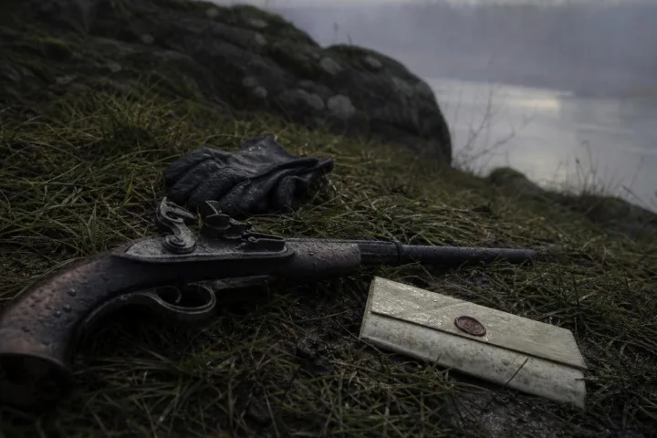 Pistola antica e lettera piegata sull’erba umida vicino a un belvedere sul fiume