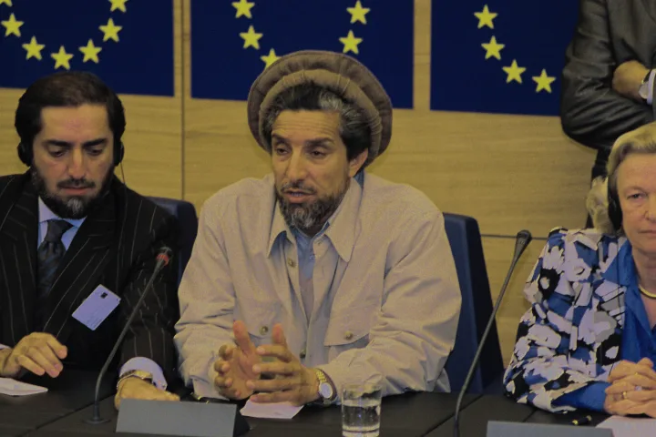 Conferenza storica di Ahmad Shah Massoud con microfoni e sguardi tesi in una sala europea